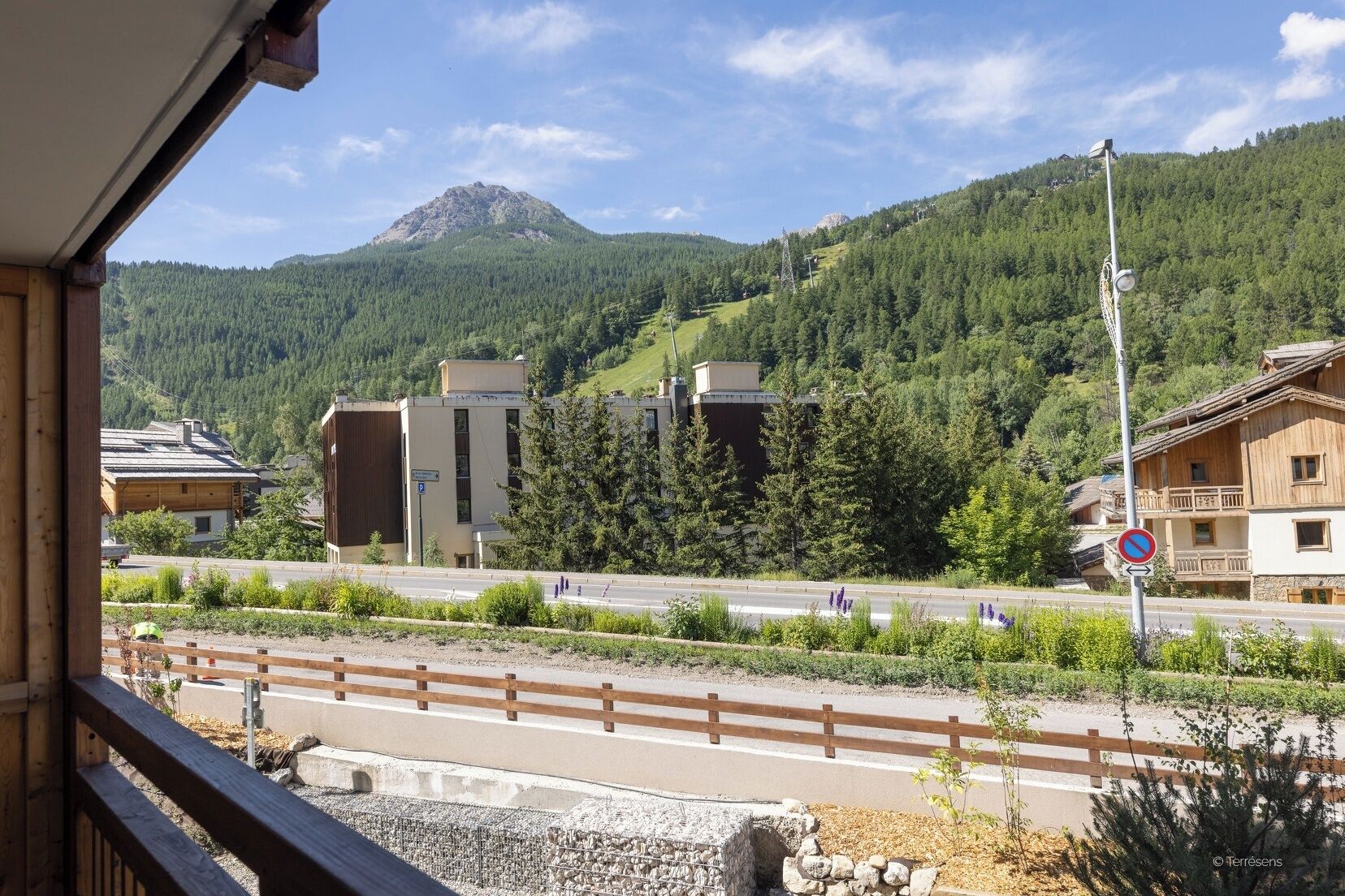 A mountain view with a road, buildings, and a no parking sign.