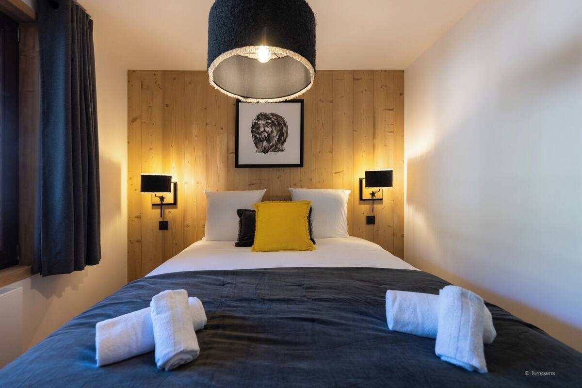 A hotel room with a bed, two bedside lamps, a framed picture on the wall, and a window with curtains.