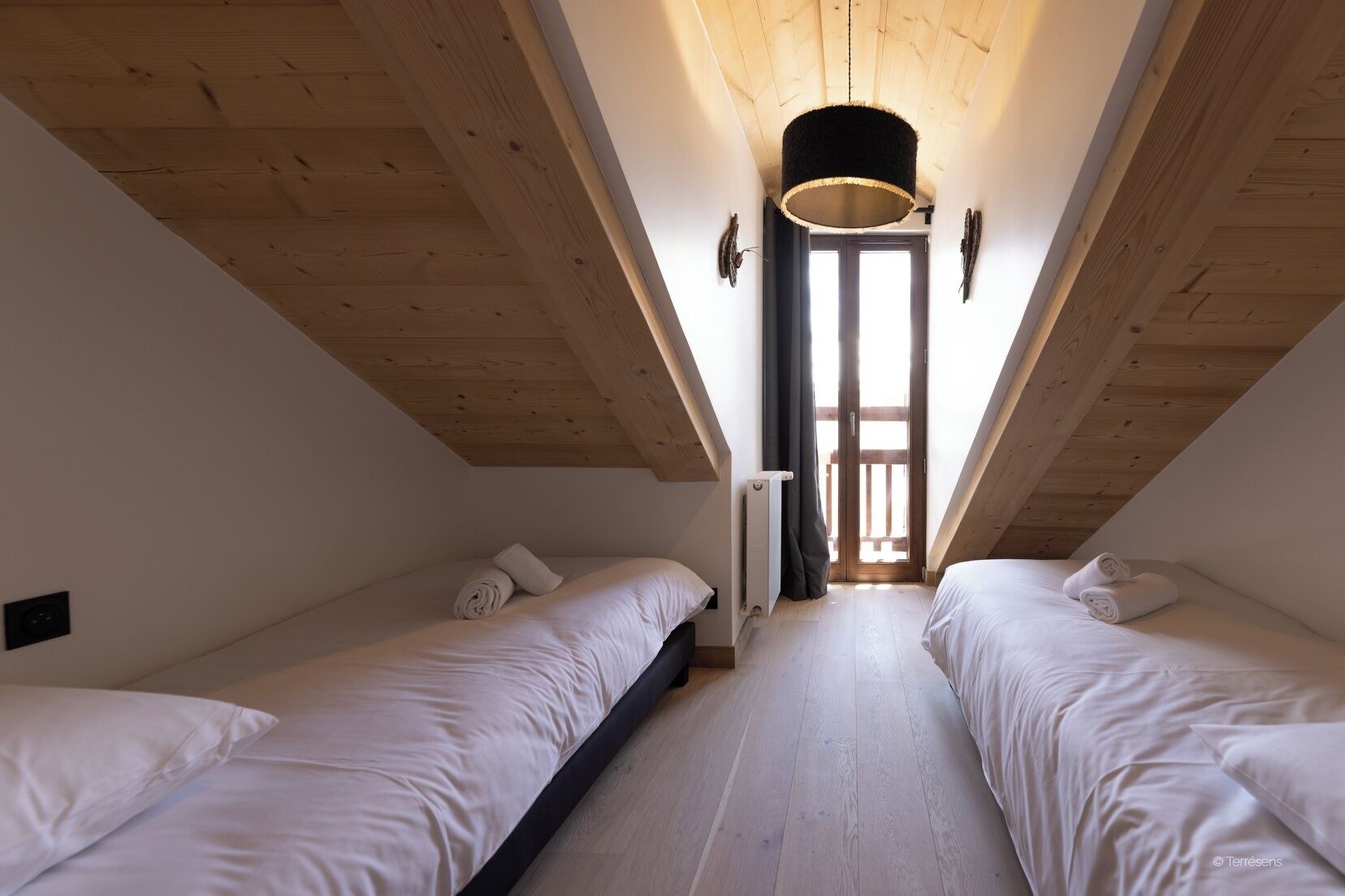 A bedroom with two beds, a radiator, and a window with curtains.
