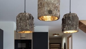 Un coin repas avec une table en bois, trois lampes suspendues au style rustique et un vase.