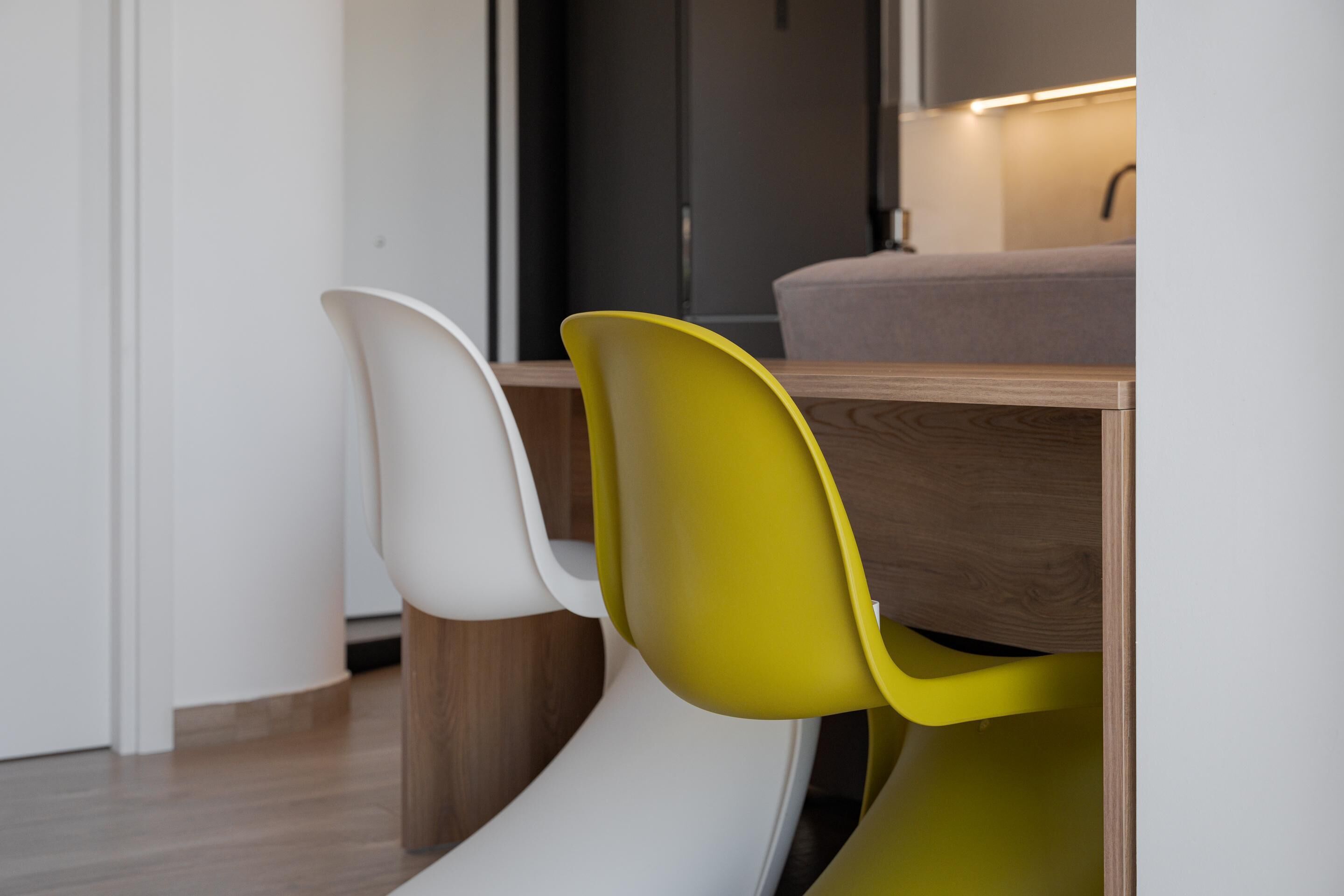 A modern dining area with a wooden table and two chairs, one white and one yellow.