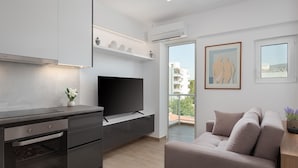 A modern kitchen with a built-in oven and a flat-screen TV. There is a balcony with a view of buildings and a painting on the wall. - Athenian Riviera Seaside Suite (Vouliagmeni)