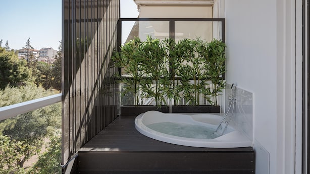 A modern balcony with a hot tub, wooden flooring, and a view of greenery and buildings. - Athenian Riviera Seaside Suite (Vouliagmeni)