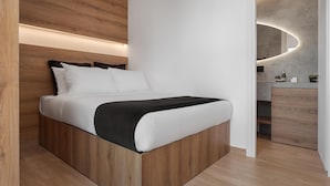 A modern bedroom with a wooden bed frame, white bedding, and a built-in bedside table with a mirror. - Athenian Riviera Seaside Suite (Vouliagmeni)