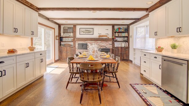 A kitchen with wooden beams, white cabinets, and a dining area with a wooden table and chairs. - Walk to Downtown Chatham, Steps to Beach! (Chatham)