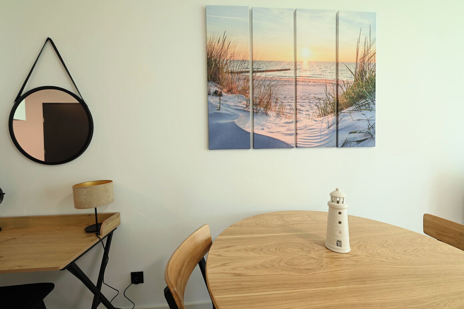 A dining area with a wooden table, chairs, a lamp, a small lighthouse model, and a wall-mounted painting of a beach scene.