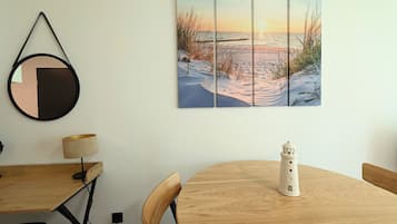 A dining area with a wooden table, chairs, a lamp, a small lighthouse model, and a wall-mounted painting of a beach scene.