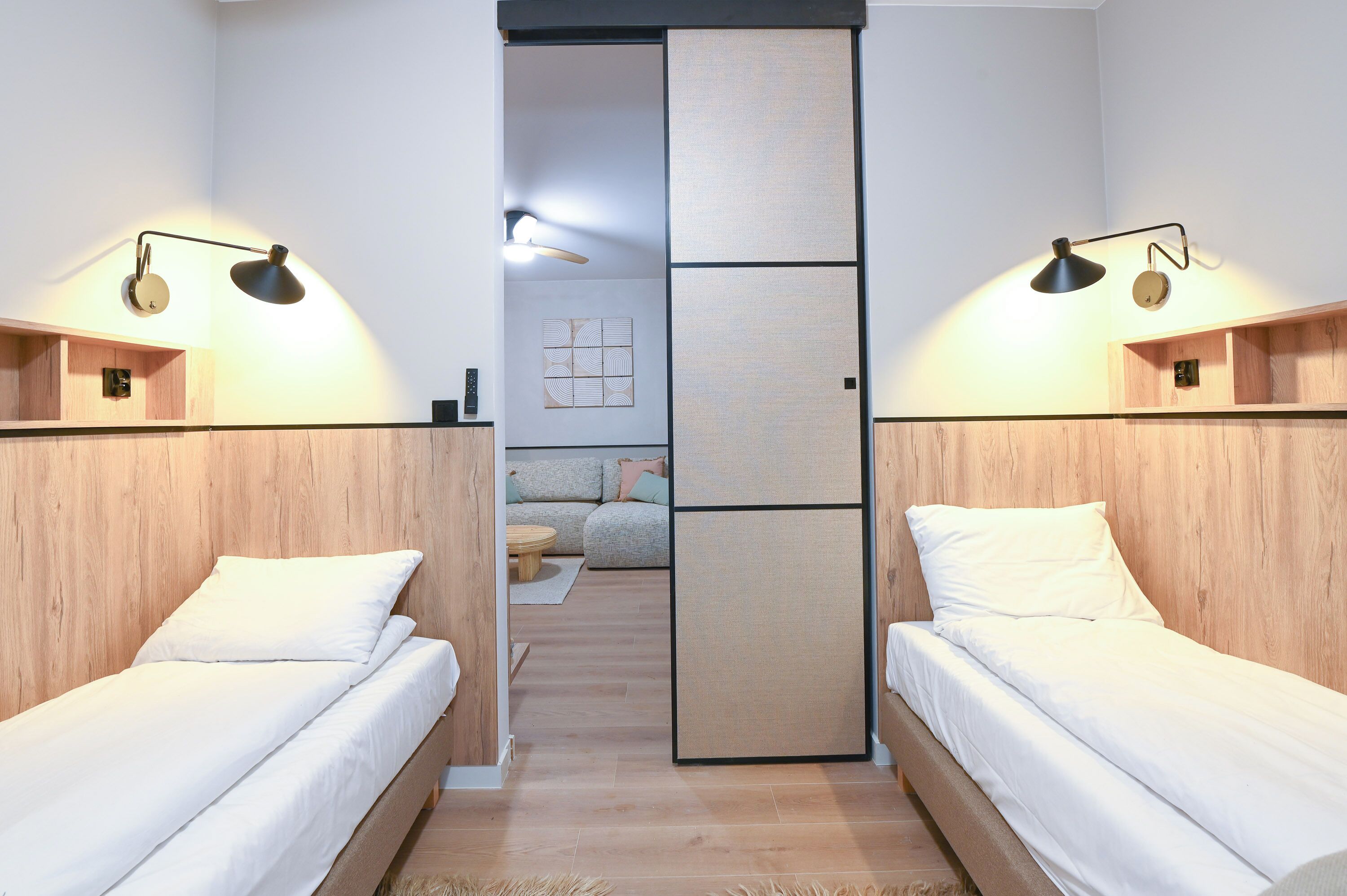 Quarto com duas camas, cabeceiras de madeira e luminárias fixadas na parede.