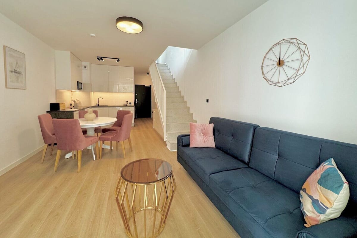 A modern living room with a dark blue sofa, a round glass coffee table, and a staircase leading to an upper level.