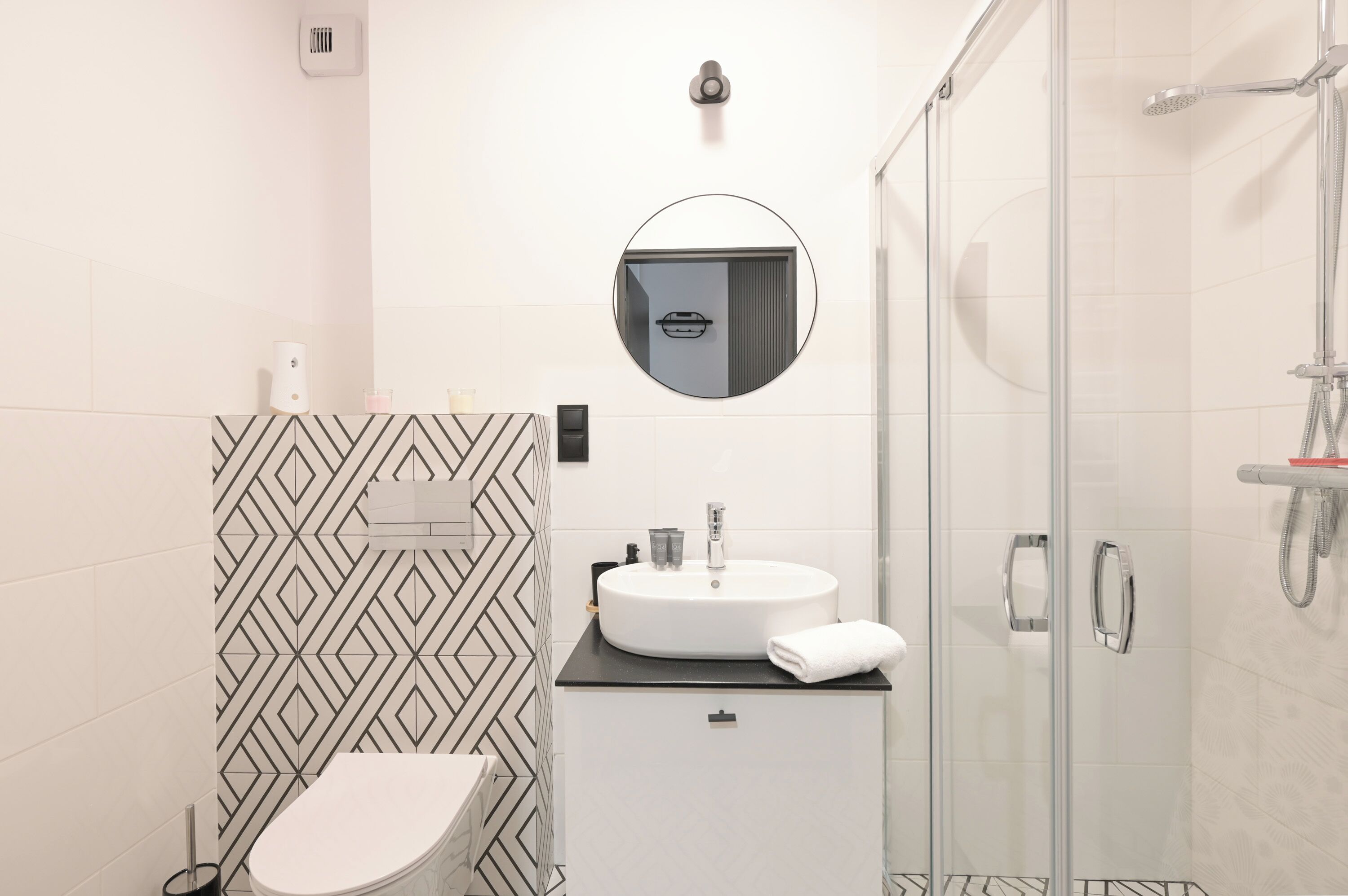 A modern bathroom with a round mirror, a sink, a toilet, and a glass-enclosed shower.
