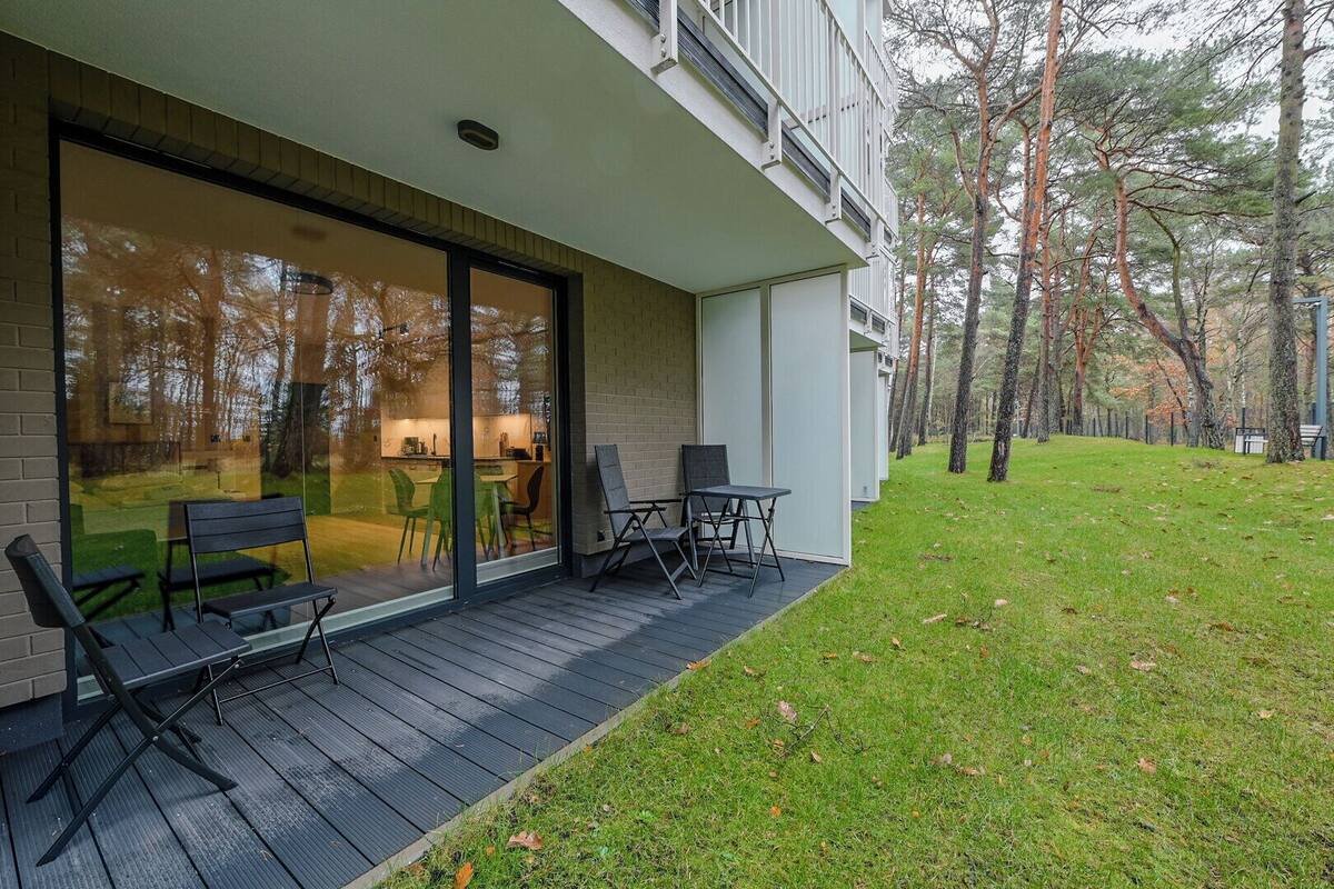 A modern building with a glass facade, outdoor seating, and a grassy area with trees.