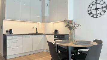 A modern kitchen with white cabinets, a round dining table with black chairs, and a wall clock.