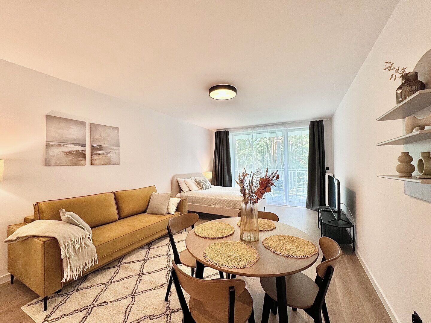 Ein gemütliches Wohnzimmer mit einer Couch, einem Esstisch mit Platzsets und Blick auf einen Balkon.