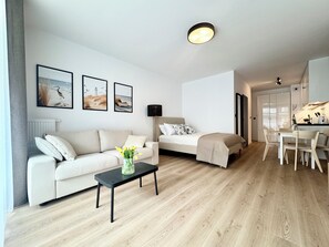 A modern, well-lit living room with a sofa, a coffee table, and a bed. There are framed pictures on the wall and a small table with a vase of flowers. - Nadmorska Florina by Q4Apartments (Leba)