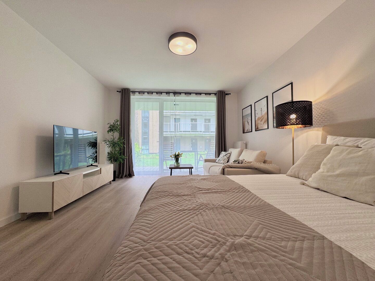 Ein modernes Hotelzimmer mit einem großen Bett, einem Flachbildfernseher, einem Nachttisch, einer Lampe und Blick ins Freie.