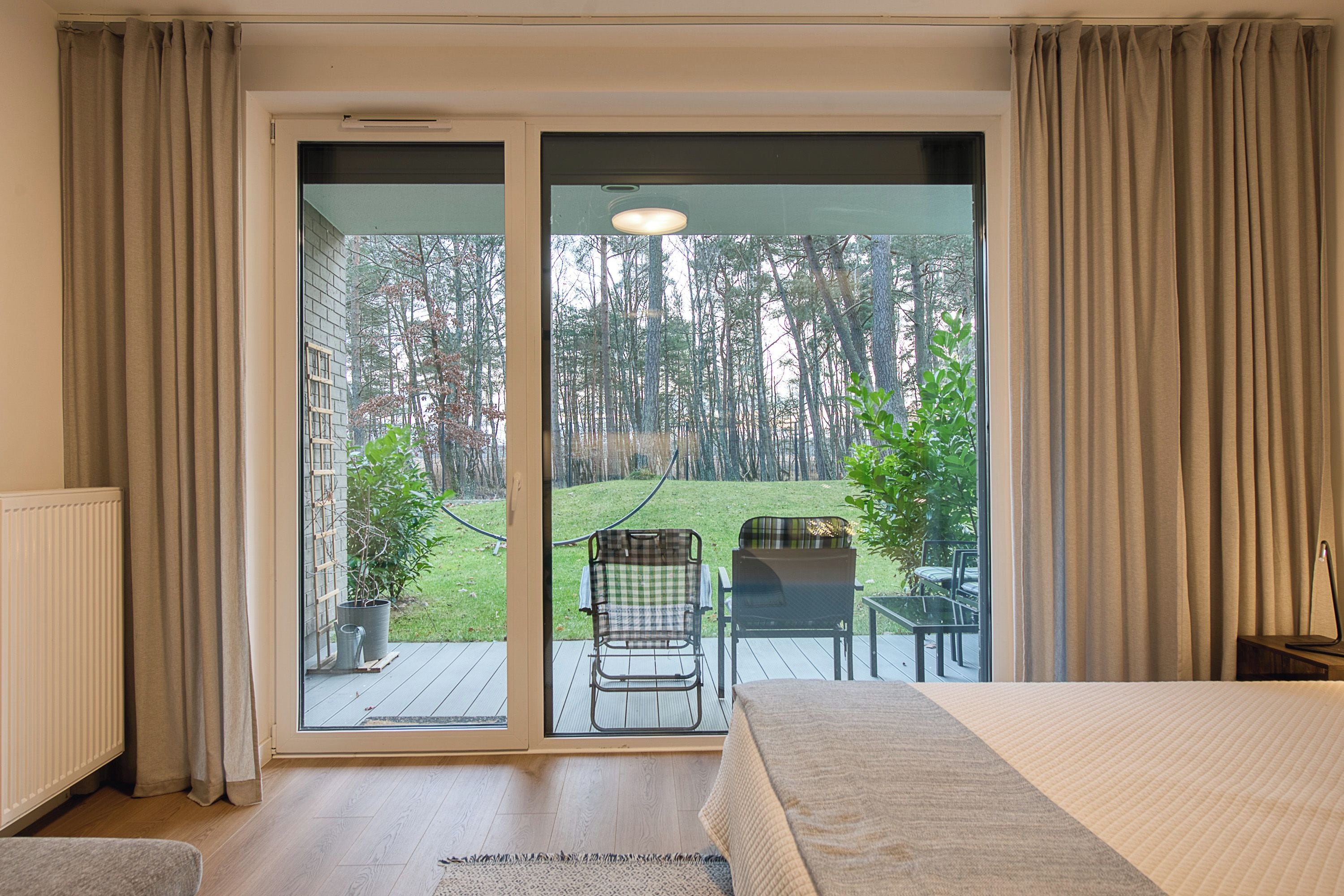 Ein Schlafzimmer mit einer großen Schiebeglaswand, die auf eine Terrasse mit einem Stuhl und einem kleinen Tisch führt.