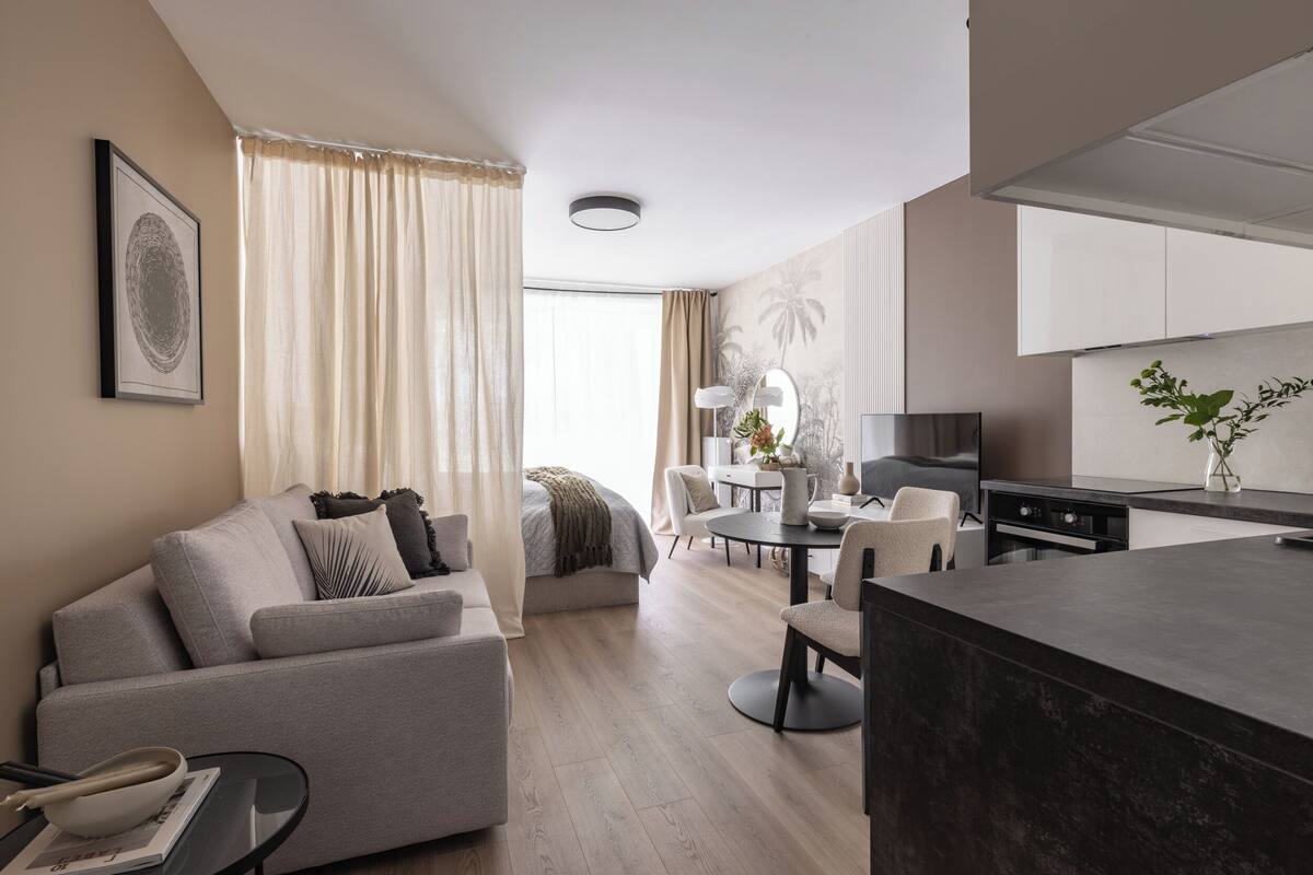 A modern living room with a sofa, a dining table, and a kitchen area.