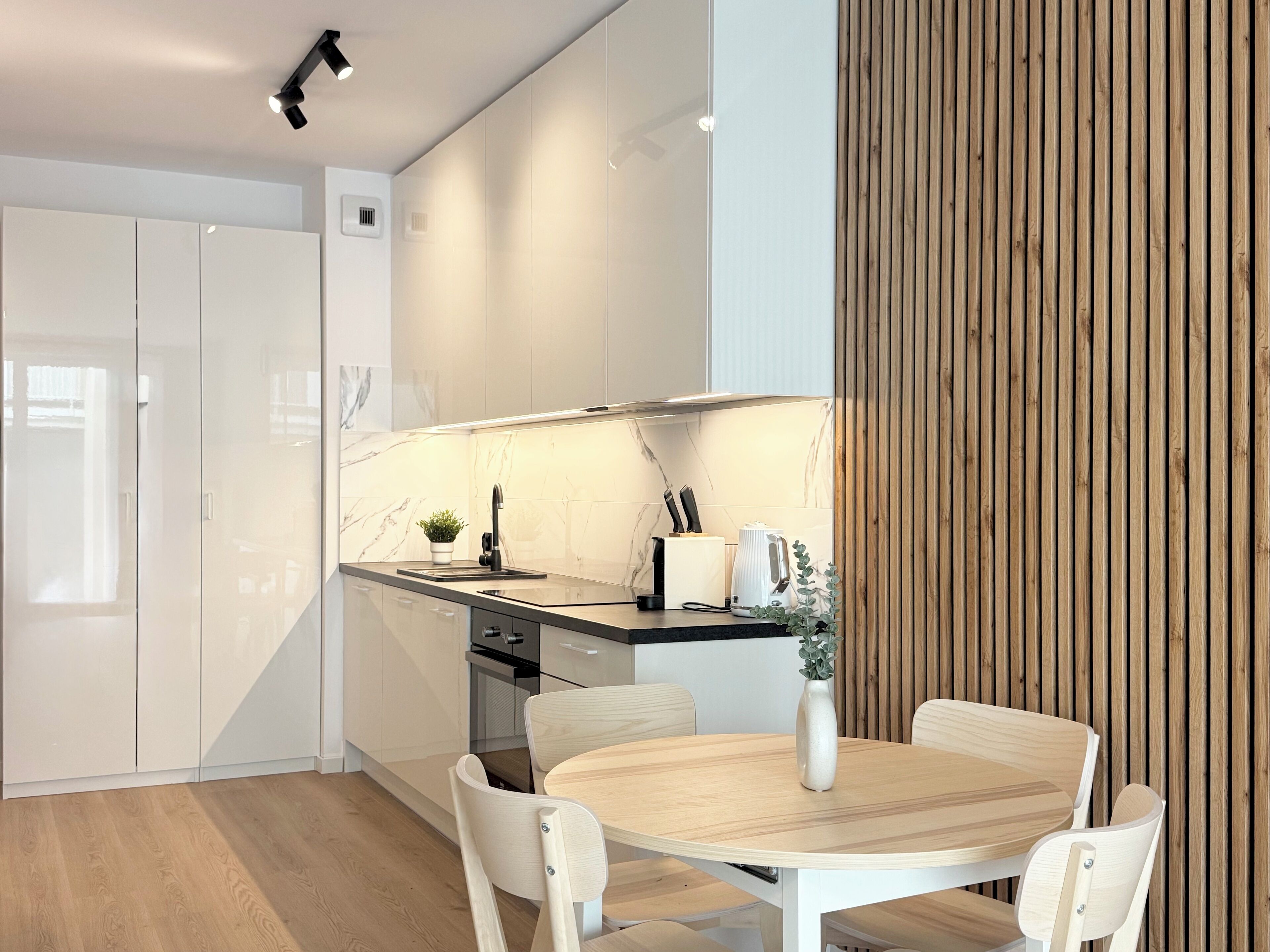 Una cocina moderna con armarios blancos, salpicadero de mármol y una pared decorativa de madera.