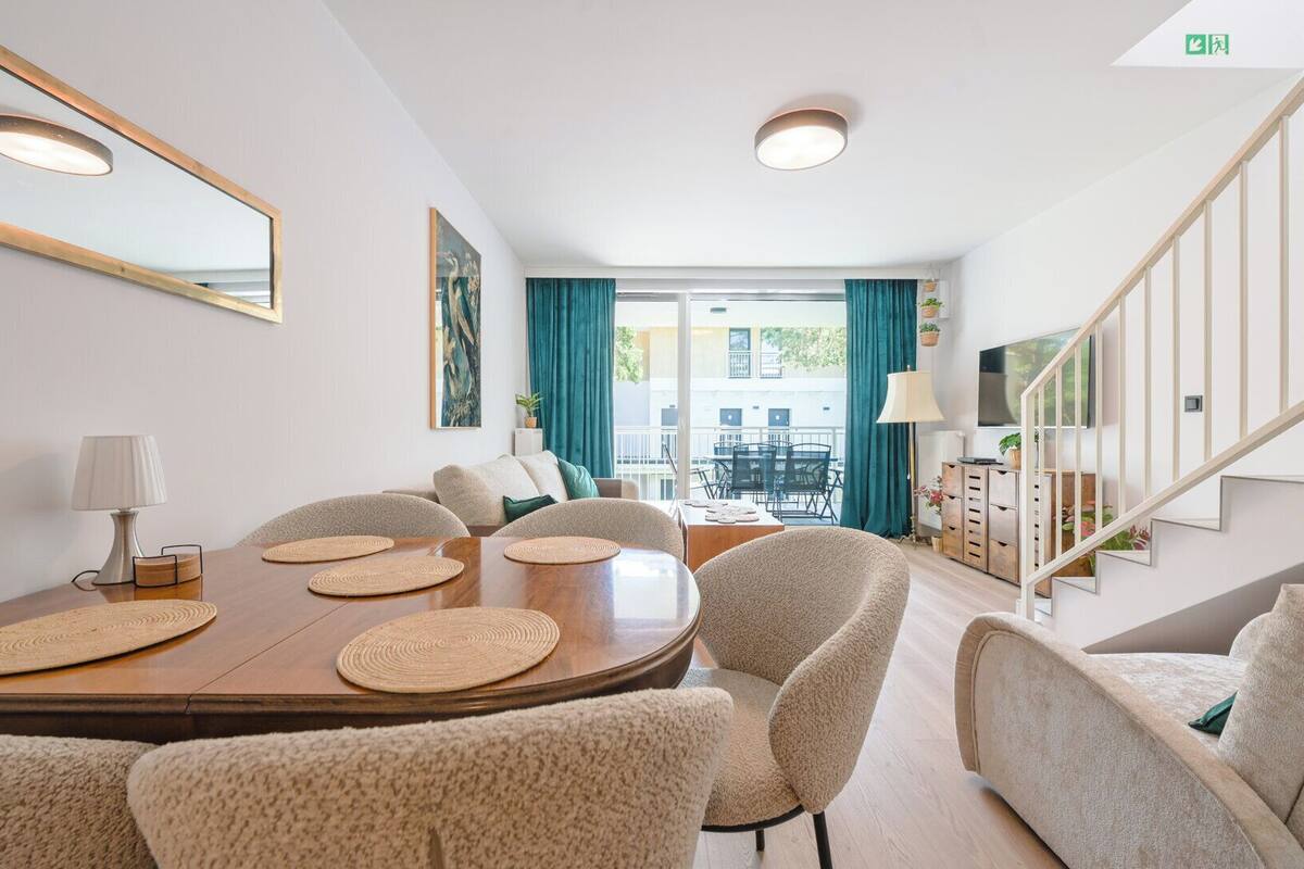 A modern living room with a dining area, a staircase, and a balcony with a view.
