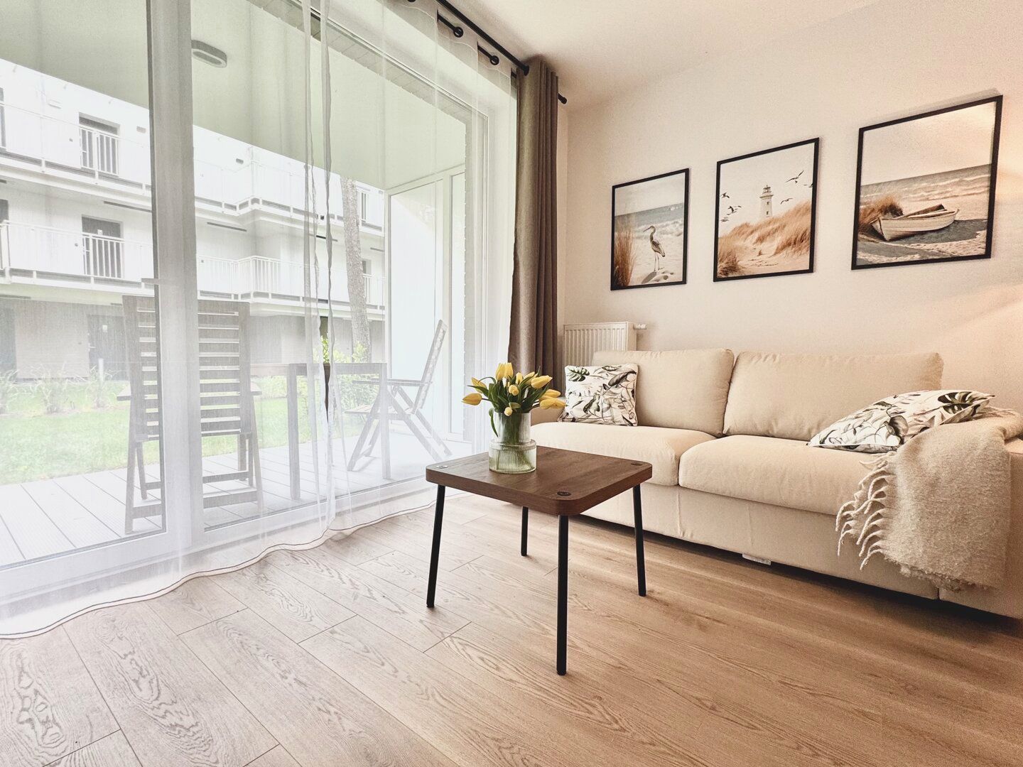 A living room with a sofa, a coffee table with a vase of flowers, and a large sliding glass door leading to an outdoor area.