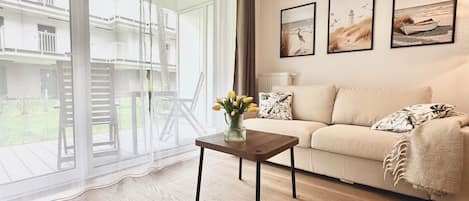 Ein Wohnzimmer mit einer Couch, einem Couchtisch mit Blumen und einer großen Schiebeglastür, die zu einem Außenbereich führt.