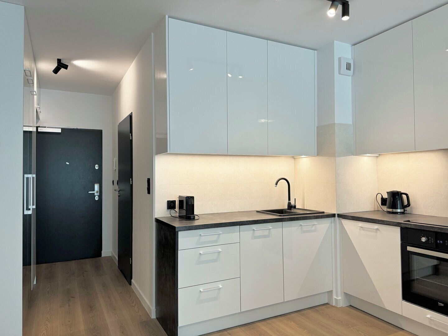 A modern kitchen with white cabinets, a black countertop, a sink, a coffee maker, and an oven.