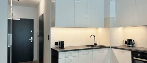 A modern kitchen with white cabinets, a black countertop, a sink, a coffee maker, and an oven.