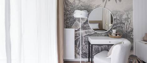 Une chambre à coucher moderne avec une coiffeuse blanche, un miroir rond, une chaise blanche et un papier peint à motifs tropicaux.