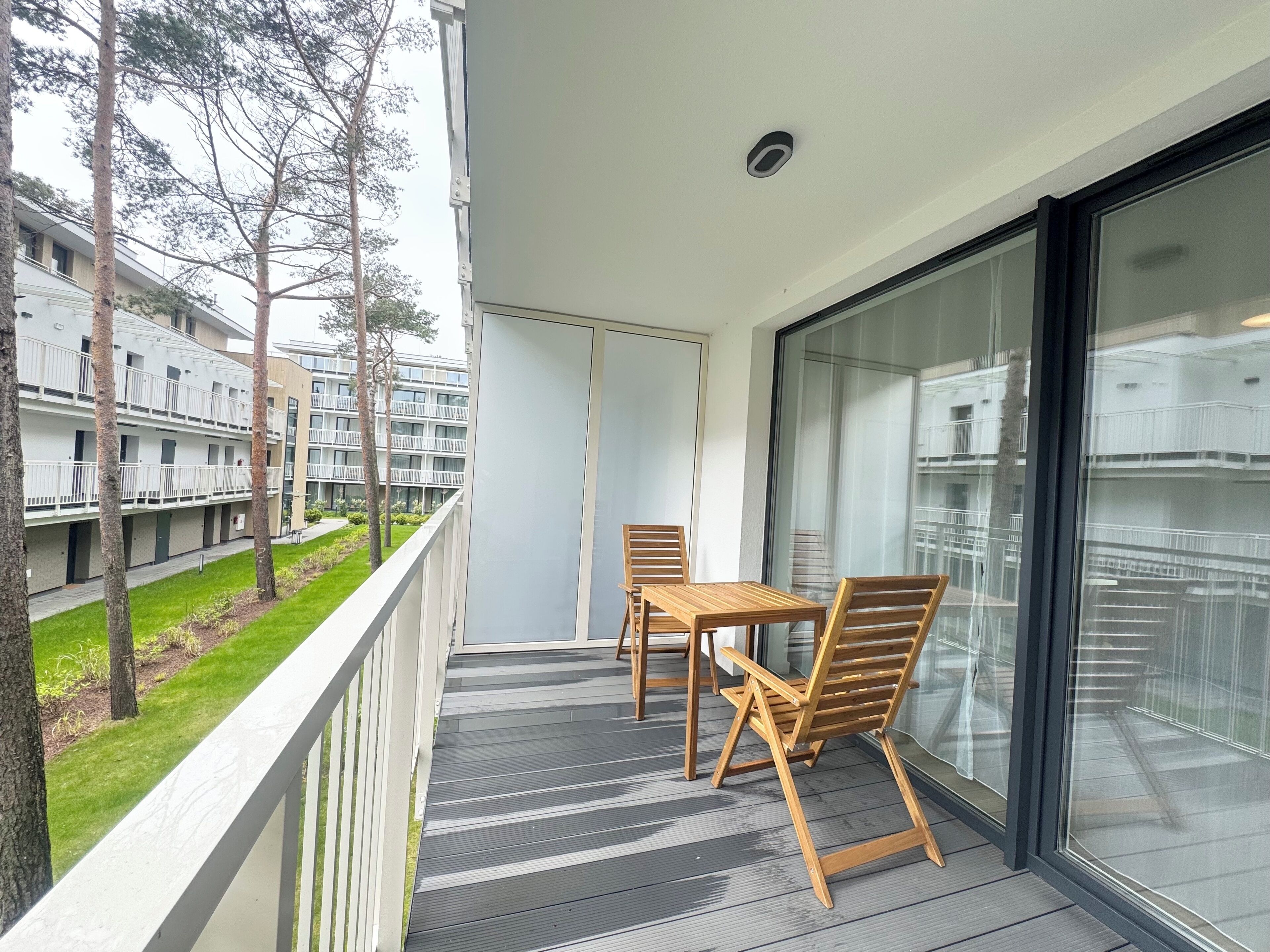 A balcony with a table and chairs, overlooking a residential building and a grassy area.