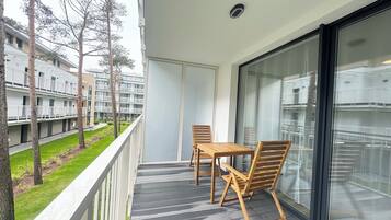 A balcony with a table and chairs, overlooking a residential building and a grassy area.