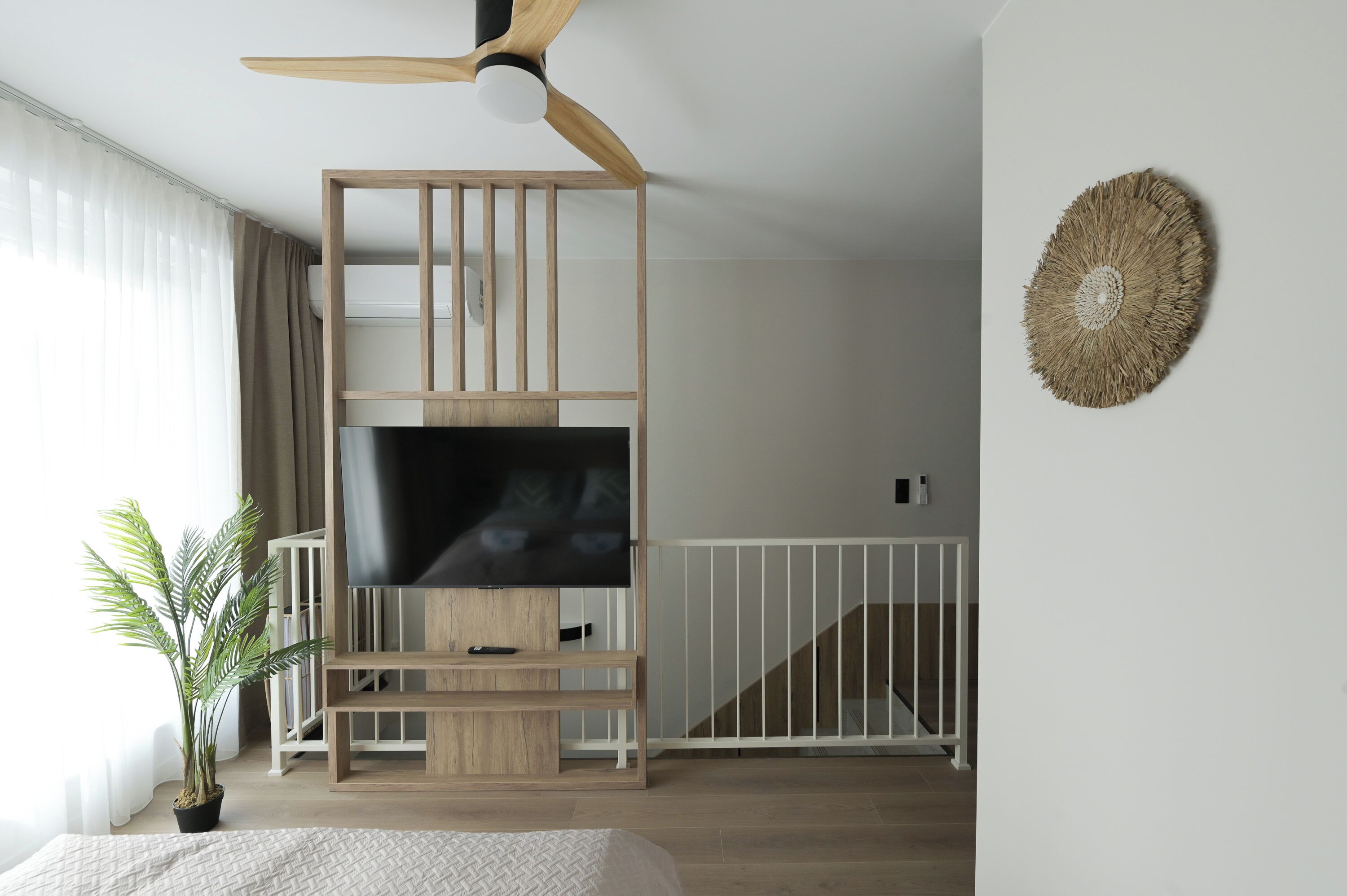 Una habitación moderna con un televisor sobre un mueble de madera, un ventilador de techo, una escalera y un objeto decorativo en la pared.