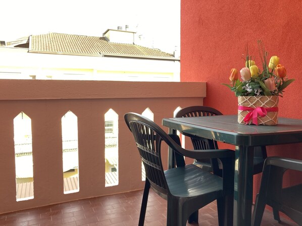 Un balcon avec une table et des chaises, un vase de fleurs et un mur rouge.