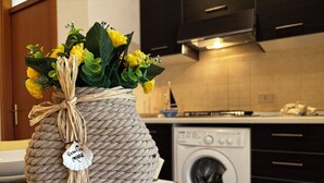 A kitchen with a washing machine, dark cabinets, and a table with a floral tablecloth. - Comfortable flat in Bibione - Beahost (Rosolina Mare)