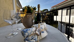 A round table with two wine glasses, a bottle of champagne, a woven basket with flowers, and a cloth with a blue pattern. - Renovated apartment in Rosolina (Rosolina Mare)