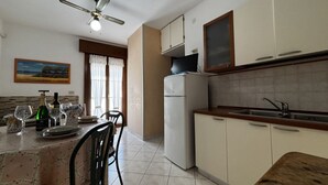 A compact kitchen with a refrigerator, a microwave, and a sink. There is a dining table with chairs and a ceiling fan above. - Renovated apartment in Rosolina (Rosolina Mare)