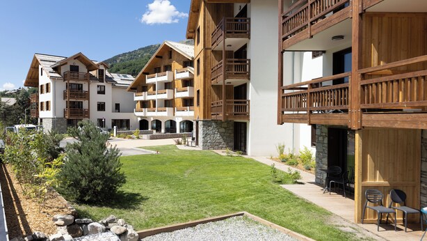 A modern hotel with multiple balconies, a well-maintained lawn, and a stone facade. - TERRESENS - Hôtel Le Cristal Lodge (Saint-Chaffrey)