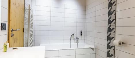 A modern bathroom with white tiles, a bathtub, a wooden door, and a towel rack.