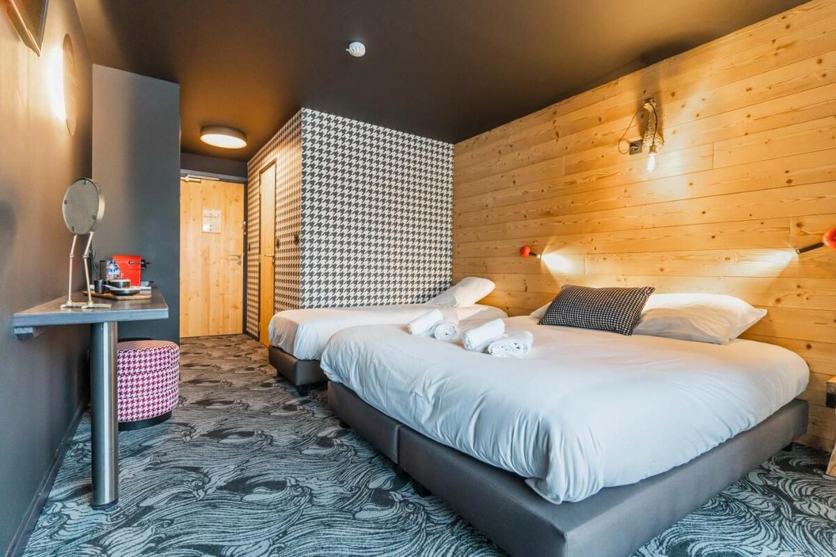Ein modernes Hotelzimmer mit einem großen Bett, einem kleinen Tisch mit Spiegel und einem gemusterten Teppich.