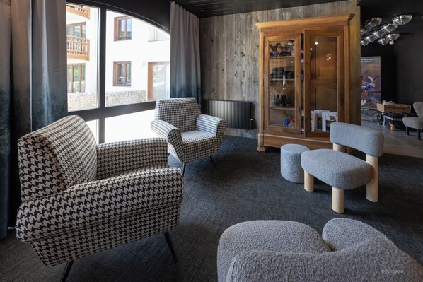 Un salon moderne avec des fauteuils à motif pied-de-poule, un pouf gris et un meuble en bois doté de portes en verre.