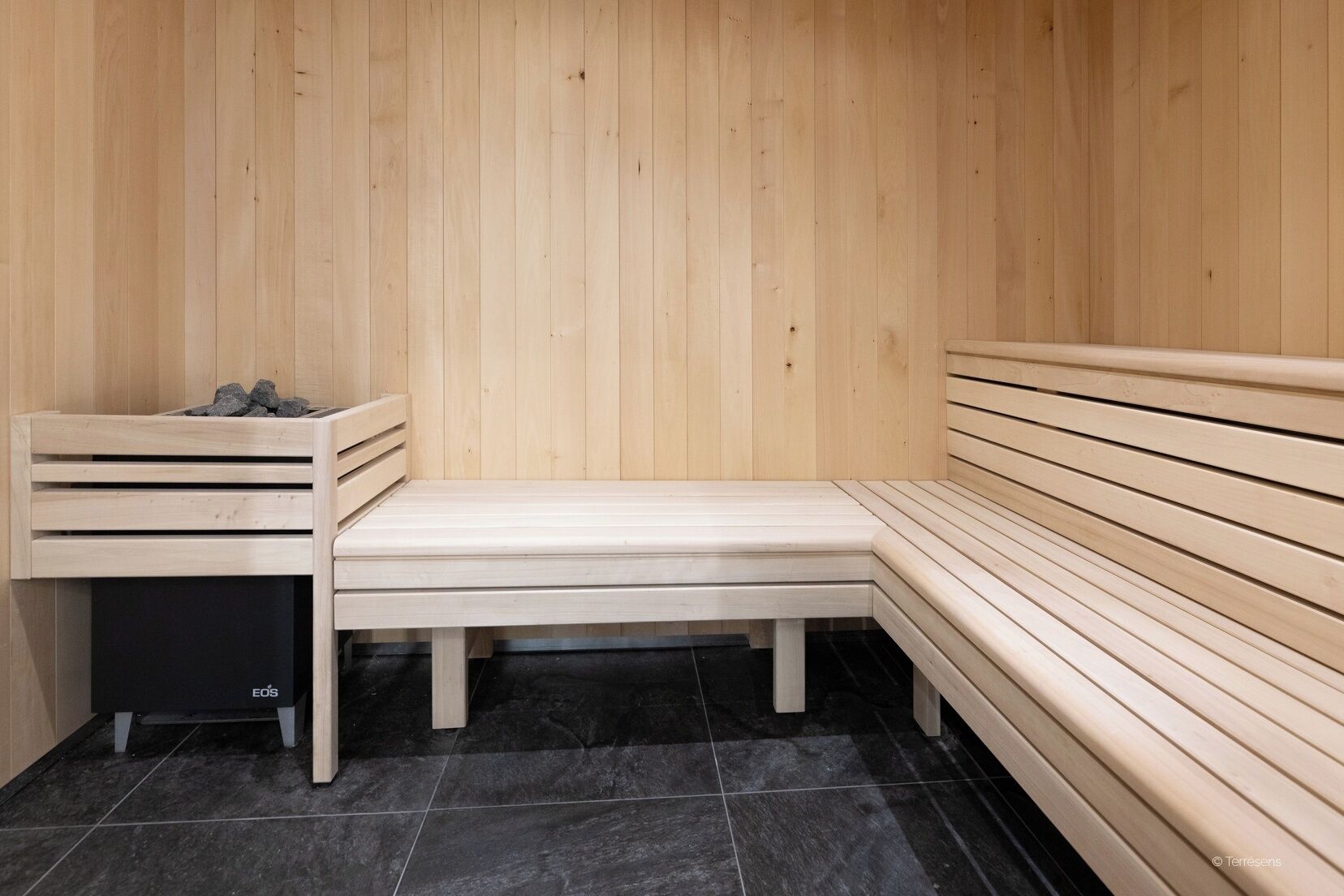 A sauna room with a wooden bench, a bench with a backrest, and a black trash bin labeled "EOS".