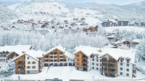 A snow-covered resort with multiple wooden buildings, a ski slope, and a mountainous backdrop. - TERRESENS - Hôtel Le Cristal Lodge (Saint-Chaffrey)