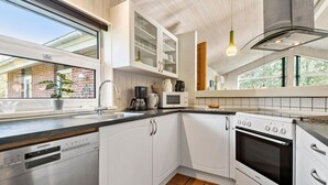 Una cucina moderna con mobili bianchi, lavastoviglie, microonde, fornello e una finestra vista un edificio in mattoni.