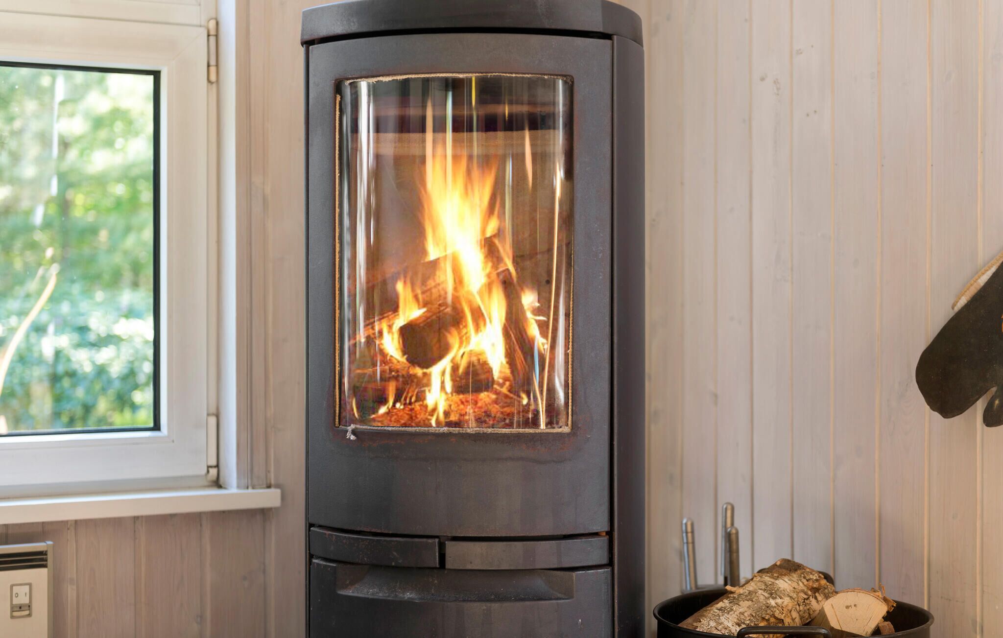 A wood-burning stove with a glass front, a window to the left, and a metal door to the right.