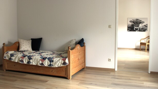 Un dormitorio con cama de madera, colcha y una puerta que da a otra habitación.