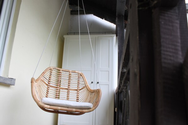 A wicker hanging chair with a cushion, suspended by ropes, in front of a white door.