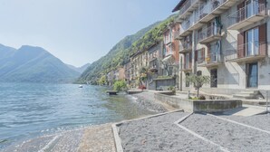 A lakeside hotel with a rocky shoreline, balconies, and a view of mountains.