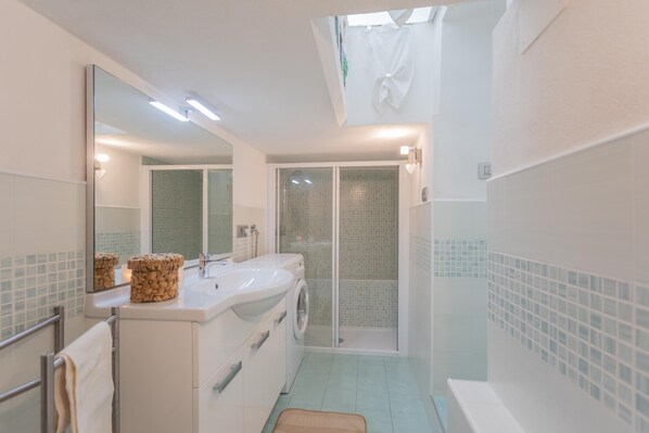 Un baño moderno con un espejo grande, un lavabo, una lavadora y una zona de ducha.