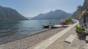 A lakeside walkway with pebbles, a bench, and a small garden area.
