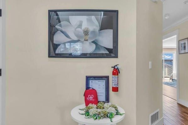 Una obra de arte abstracta enmarco, un extintor y una pequeña mesa con un arreglo floral en el vestíbulo de un hotel.