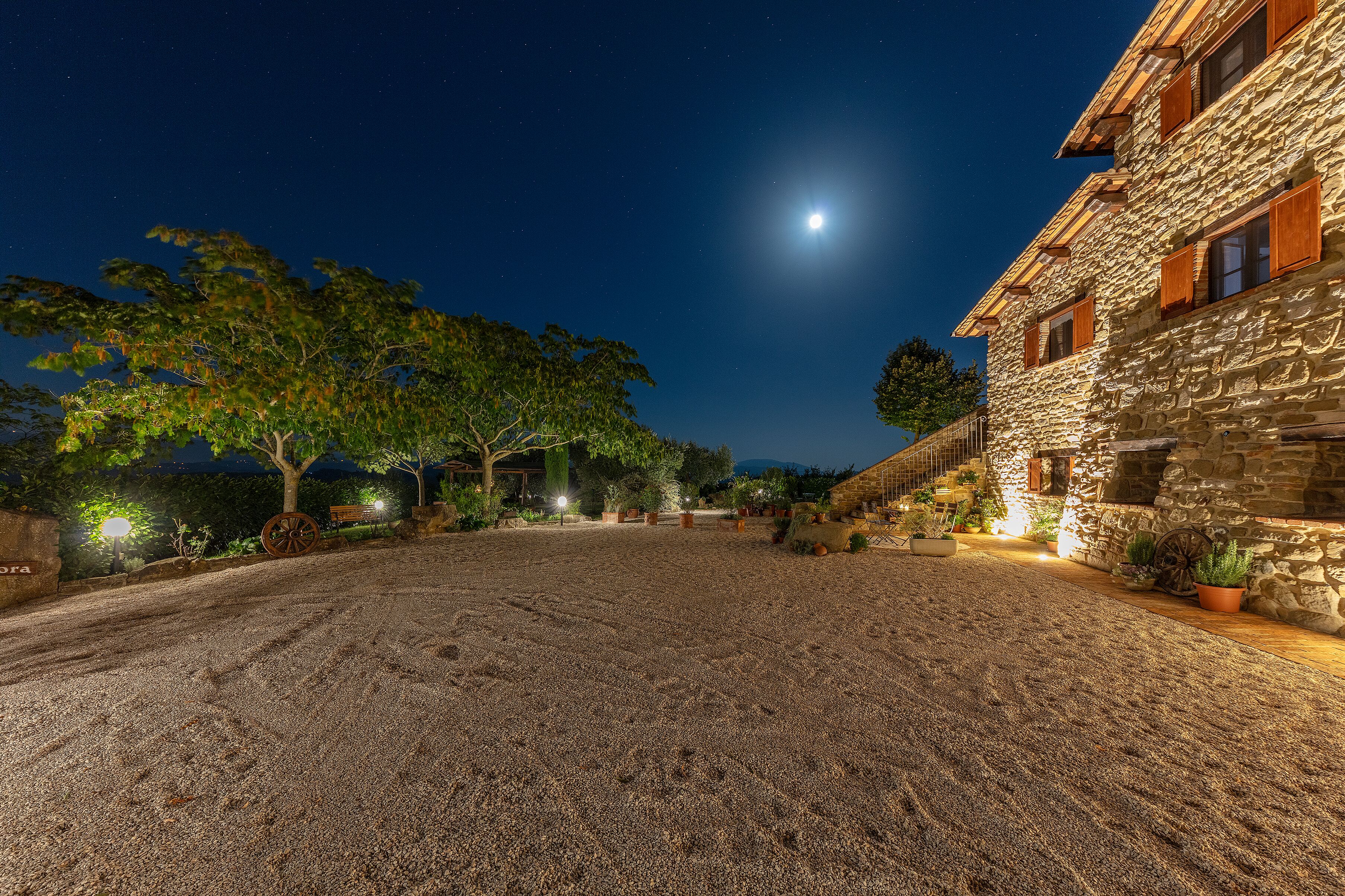 A stone building with a gravel courtyard, trees, and a night sky with a visible moon.